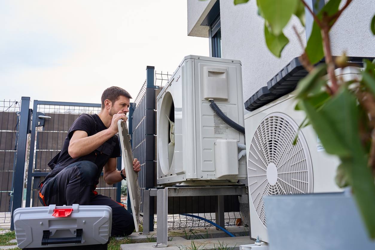 Heat pump repair technician inspecting an outdoor unit at an Islip, NY home